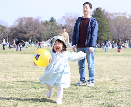 ボールを持って走る女の子と見守る父親の写真
